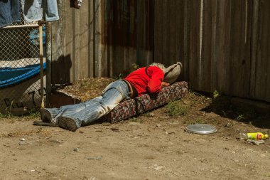 Varna, Ukrayna - 2017 yaklaşık: Bilinmeyen evsiz adam liman dolgu üzerinde uyuyor. Evsiz bir adam yere yaz gününde uyur ve Avrupa Birliği'ndeki ip, eski yırtık pırtık şeyler kurur