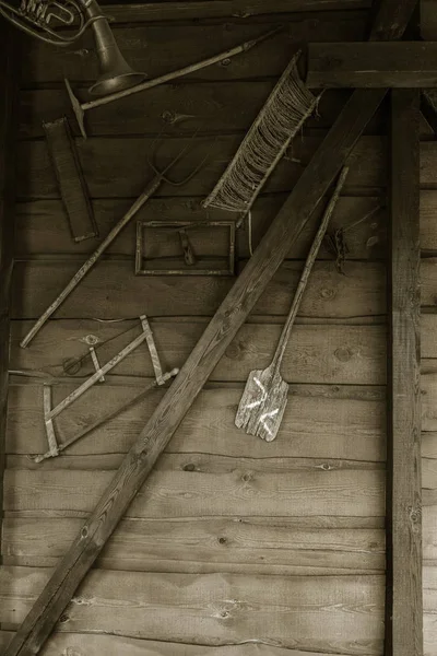 The old traditional Russian interior of the room, the ancient wooden tools of peasant labor hang on the wooden wall of the house. Antique items of household utensils of ancient farmers