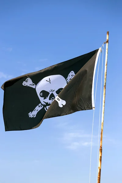 海賊団のシンボルとして 頭蓋骨を描いた旗のフラグメント ジョリーロ ジャー スカルとクロスボーン海賊フラグ青い空を背景に引き裂かれた風 空に風に吹かれて陽気なロジャーや海賊旗 — ストック写真