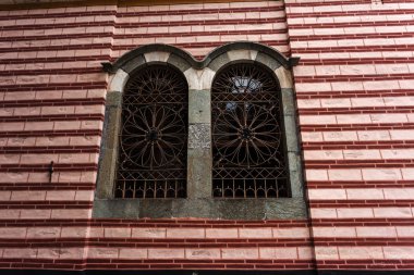 Eski bir dövme demir ızgara, dekoratif güvenlik öğesi. Güzel tuğla duvar resimleri ile eski bir ev pencere eski bir ızgara. Klasik metal kafes sahte. Renkli tuğla duvar