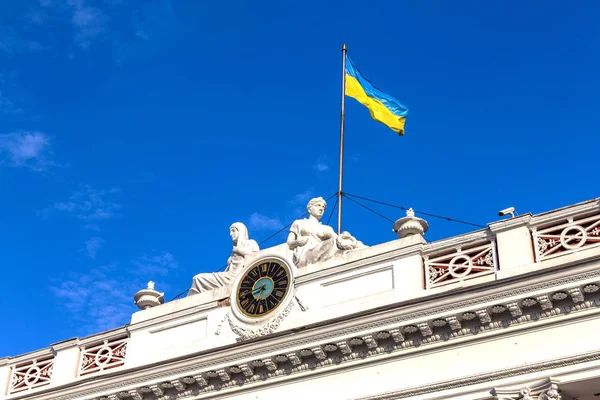 facade of the building official Odessa City Hall with the city's main clock and the Ukrainian flag on a background of bright blue sky