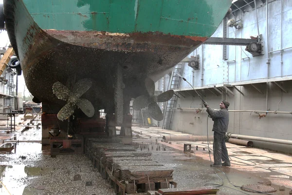 ODESSA - April 15, 2014: Work in dry dock with water jet cleans the bottom of the ship from sea vegetation and mussel colonies during routine overhaul on outdated manual technology