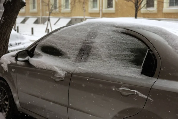 Strong snowfall in city streets in winter. Cars are covered with snow, slippery road. Bad weather in winter: heavy snow and blizzard. Pedestrians go under heavy snow. Winter and snowstorm, snowfall