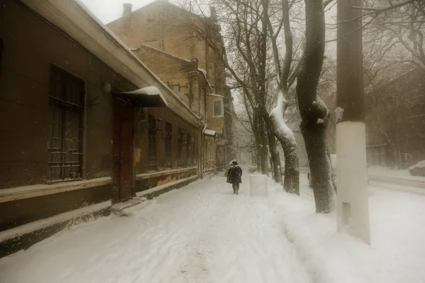 Strong snowfall in city streets in winter. Cars are covered with snow, slippery road. Bad weather in winter: heavy snow and blizzard. Pedestrians go under heavy snow. Winter and snowstorm, snowfall