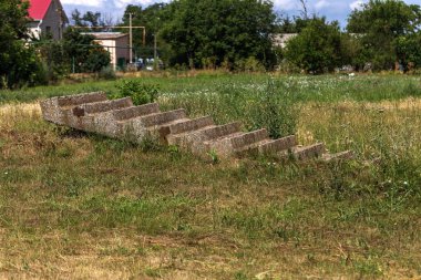 Terk edilmiş eski gereksiz beton merdivenin yalnız otların arasında yatıyor. Merdiven nereye gittiğimizi bilmeden gökyüzüne. Eski taş basamaklar çöp çöplükte terk merdiven parçasının kaşıdı. Beton merdiven