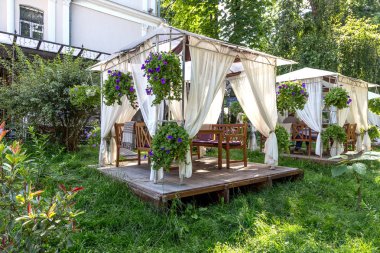 Ahşap bir platformda bir gölgelik altında sokak kafe taze otların arasında şehir parkı yeşil üzerinde bulunan ve taze çiçeklerle süslenmiş.