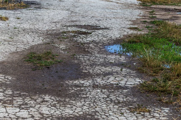 Damaged road, cracked asphalt sword with potholes and spots, Ukraine. Very bad asphalt road with large holes. Terrible technology construction roads. Numerous dangerous failures. Bad road. Road repair