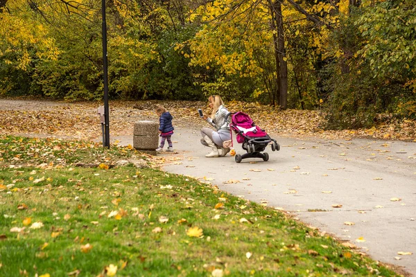 Varna, Bulgaristan - 13 Kasım 2015: sonbahar Şehir Parkı. Parlak güneşli bir günde parkta yürüyüş küçük çocuklu Genç Anne.
