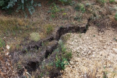 Çevreye zararlı bir bölgede dağ heyelan. Yeryüzündeki büyük çatlaklar, toprak yolu kapatan büyük katmanların inişi. Dağ yamacının yamacında baraj tehlikesi