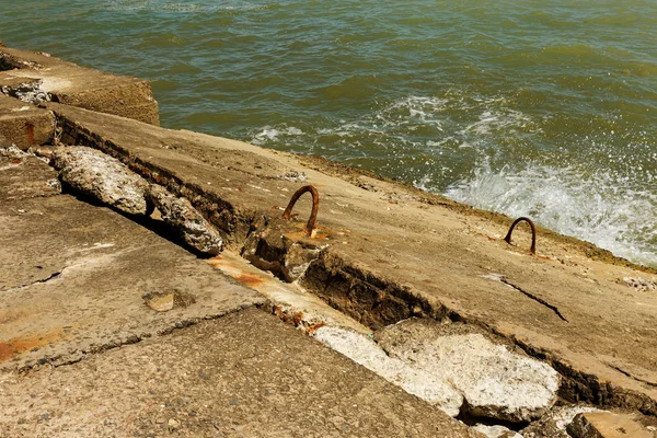Destroyed coastal concrete protective structure. Large deep cracks between slabs of blocks protect shore from erosion of impact of sea wave. Huge pieces of concrete with reinforcement to protect shore