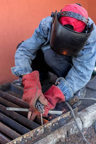 Welder at work. Welder cooks metal grate on the ground blowtorch on the ground in special clothes and mask welder. Selective Focus