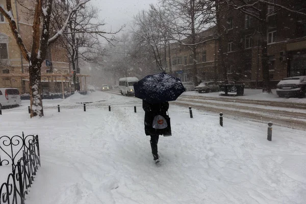 Strong snowfall in city streets in winter. Cars are covered with snow, slippery road. Bad weather in winter: heavy snow and blizzard. Pedestrians go under heavy snow. Winter and snowstorm, snowfall