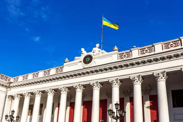facade of the building official Odessa City Hall with the city's main clock and the Ukrainian flag on a background of bright blue sky