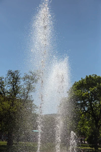 明るい晴れた日の夏の都市公園で高い水市泉 市泉の水の飛散は明るいカラフルなレインボーに太陽の光を屈折します — ストック写真