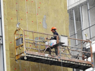 Odessa, Ukrayna - 8 Eylül 2015: cephe ısı yalıtımı yüksek katlı apartman inşaatı sırasında durdurma ve dolgu maddeleri ile çalışır. İşçiler yağmur altında çalışır. Duvarlar cephe ısı yalıtımı