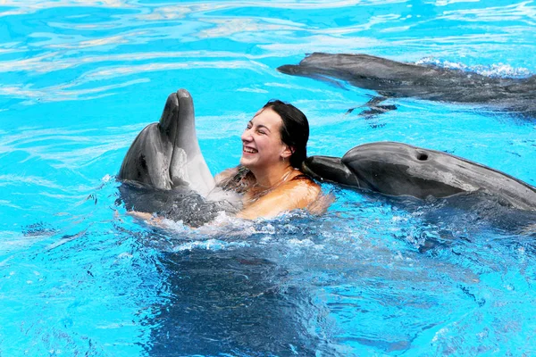 快乐年轻漂亮的女孩笑着清澈阳光明媚的日子与海豚在蓝色的游泳池里游泳 — 图库照片