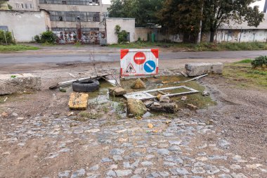 Yol ve otoyol şehrin yoksul çeyreğinde ortasına çöpe yığını büyük su birikintisi. Kapalı yol. Yolun ortasında büyük çukur su ve enkaz, arabaların tekerlekleri ile dolu. Uyarı Kaldırım Panosu