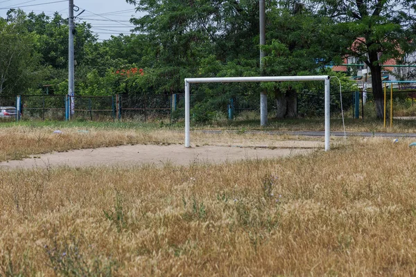 Abandoned rural stadium, not cut grass lawn field, trampled bald penalty area of a rural abandoned football field with a gate.
