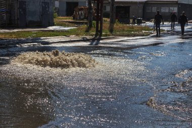 Yol kanalizasyon kapağından su akar. Lağım kanalizasyonu. Kanalizasyon sistemi kazası. Kirli lağım suyu yolda akar. Ambar çeşmesinden su akar