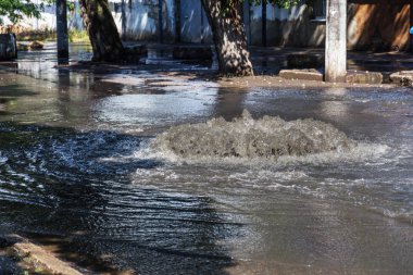 Yol kanalizasyon kapağından su akar. Lağım kanalizasyonu. Kanalizasyon sistemi kazası. Kirli lağım suyu yolda akar. Ambar çeşmesinden su akar