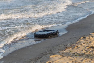 Eski siyah kauçuk lastik beach, çevre kirliliği kavramı, seçici odak, renk tonlu resim solda. Eski lastik plajda mavi su atılır. Kirliliğini ve çöplükte deniz ve plaj