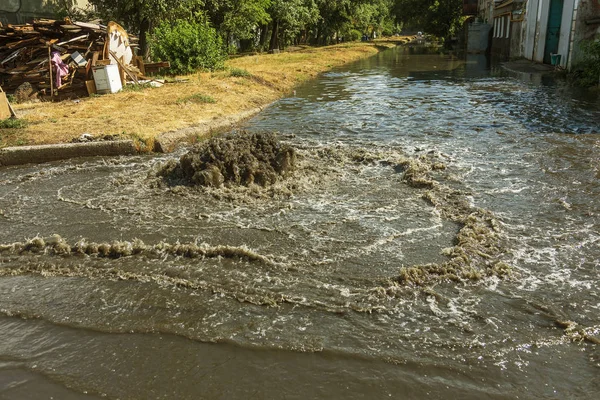 Water flows out of road sewage hatch. Drainage fountain of sewage. Accident of sewage system. Dirty sewage water flows fountain on road. From hatch fountain flows water