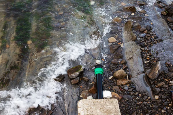 Contaminated water, sewage waste is drained through pipe into sea on an unequipped beach. Pollution of environment, ecological catastrophe. Environmental problem