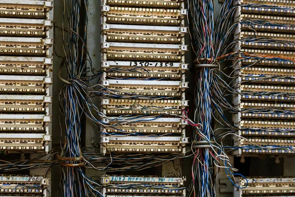 Old analog telephone switchboard in city street. Broken, looted abandoned broken old telephone switchboard wired fixed-line. Cable duct, hanging telephone wires in cabinet