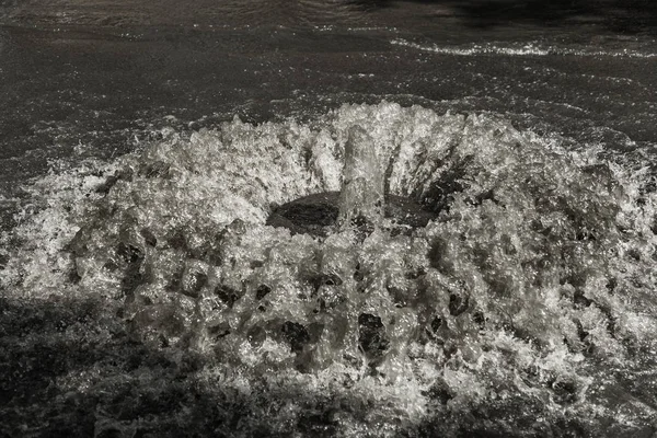 Water flows out of road sewage hatch. Drainage fountain of sewage. Accident of sewage system. Dirty sewage water flows fountain on road. From hatch fountain flows water