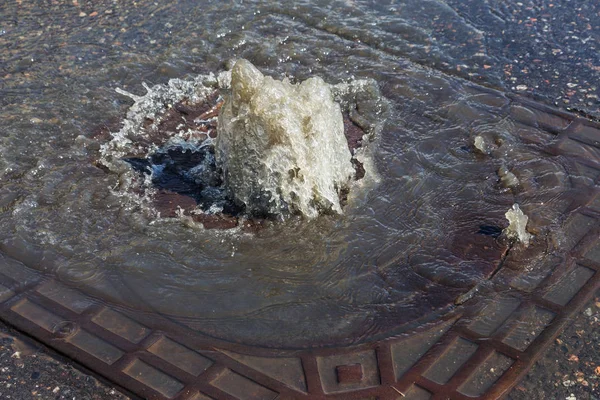 Water flows out of road sewage hatch. Drainage fountain of sewage. Accident of sewage system. Dirty sewage water flows fountain on road. From hatch fountain flows water