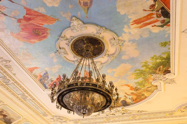 一个古色古香的老式枝形吊灯与轻蜡烛在宫殿的天花板 在彩绘天花板的背景下 剧院礼堂天花板上的老式青铜大吊灯 — 图库照片