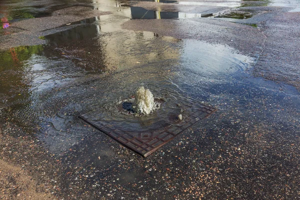 Water flows out of road sewage hatch. Drainage fountain of sewage. Accident of sewage system. Dirty sewage water flows fountain on road. From hatch fountain flows water