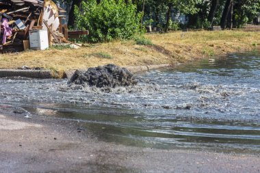 Yol kanalizasyon kapağından su akar. Lağım kanalizasyonu. Kanalizasyon sistemi kazası. Kirli lağım suyu yolda akar. Ambar çeşmesinden su akar