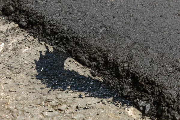 Construction of an automobile city road. New asphalt on road. Beautiful Flows of fresh liquid, hot bitumen when laying new asphalt. Abstract bitumen flows in graffiti style on asphalt