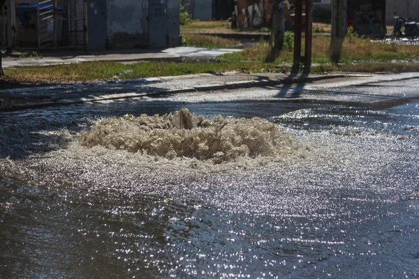 Water flows out of road sewage hatch. Drainage fountain of sewage. Accident of sewage system. Dirty sewage water flows fountain on road. From hatch fountain flows water