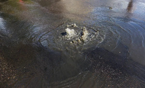 Water flows out of road sewage hatch. Drainage fountain of sewage. Accident of sewage system. Dirty sewage water flows fountain on road. From hatch fountain flows water