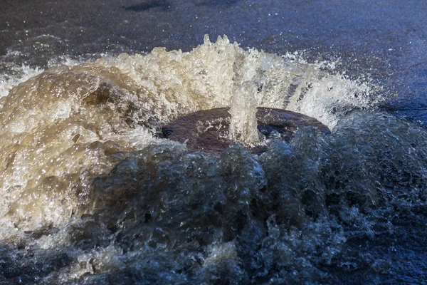 Water flows out of road sewage hatch. Drainage fountain of sewage. Accident of sewage system. Dirty sewage water flows fountain on road. From hatch fountain flows water