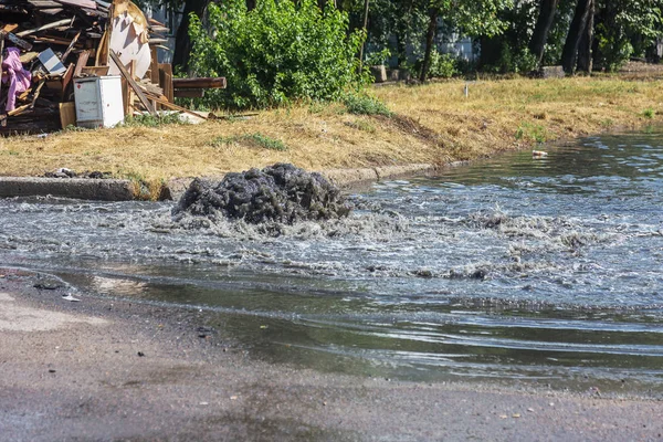 Water flows out of road sewage hatch. Drainage fountain of sewage. Accident of sewage system. Dirty sewage water flows fountain on road. From hatch fountain flows water