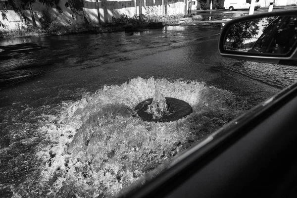 水は道路下水のハッチから流れます 下水の排水噴水 下水システムの事故 汚れた下水は道路上の噴水を流れる ハッチの噴水から水が流れる — ストック写真