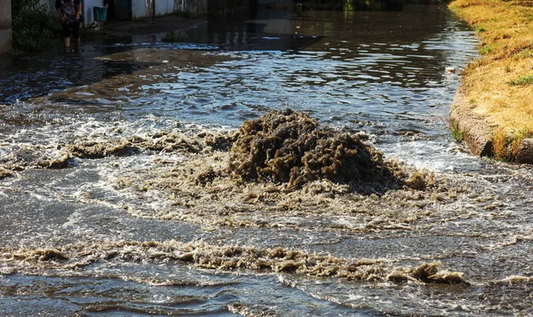 Water flows out of road sewage hatch. Drainage fountain of sewage. Accident of sewage system. Dirty sewage water flows fountain on road. From hatch fountain flows water