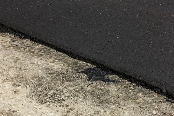 Construction of an automobile city road. New asphalt on road. Beautiful Flows of fresh liquid, hot bitumen when laying new asphalt. Abstract bitumen flows in graffiti style on asphalt