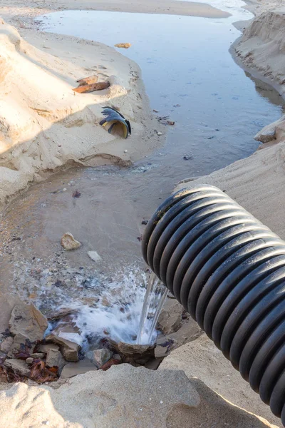 Industrial wastewater, the pipeline discharges liquid industrial waste into the sea on a city beach. Dirty sewage flows from a plastic sewer pipe onto the sand of a sea city beach