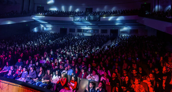 Odessa, Ukraine - April 12, 2019: Crowd of spectators at rock concert ALEKSEEV during music show. Crowds of happy people enjoy rock concert, raise their hands and clap their hands, audience on podium