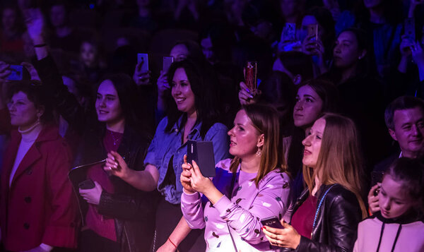 Odessa, Ukraine - April 12, 2019: Crowd of spectators at rock concert ALEKSEEV during music show. Crowds of happy people enjoy rock concert, raise their hands and clap their hands, audience on podiu