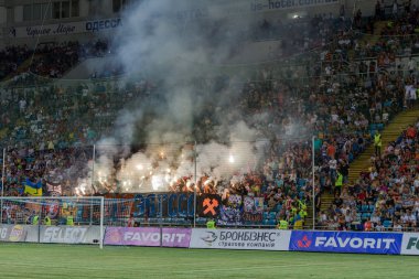 Odessa, Ukrayna -Temmuz28,2019: Fanatik taraftarlar ebedi rakipleri oyun sırasında standında. Raflarda hayranları mutlu, ateş ve bayrak sallayarak parlıyor. Stadyumda ateşli bir gösteri. Holigan ışık ateşli flaş Fan