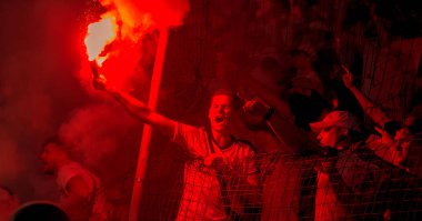 Odessa, Ukrayna -Temmuz28,2019: Fanatik taraftarlar ebedi rakipleri oyun sırasında standında. Raflarda hayranları mutlu, ateş ve bayrak sallayarak parlıyor. Stadyumda ateşli bir gösteri. Holigan ışık ateşli flaş Fan