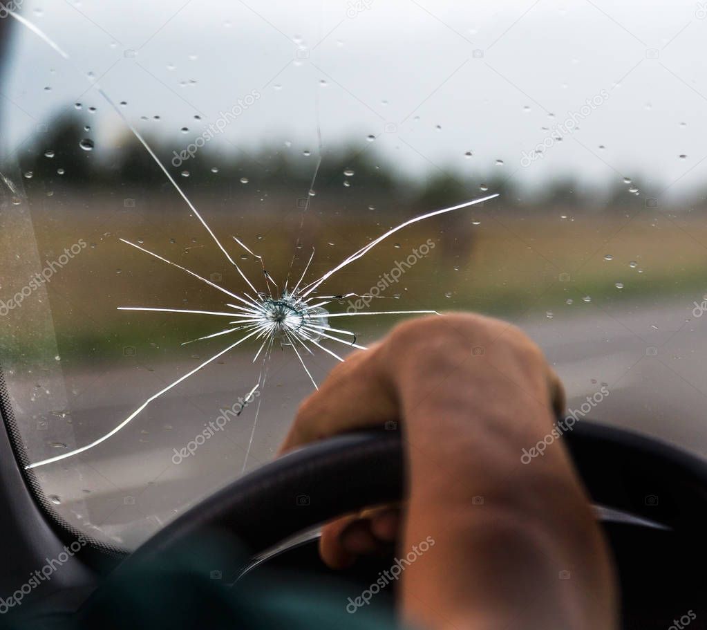 Broken windshield of a car. A web of radial splits, cracks on the triplex windshield. Broken car windshield, damaged glass with traces of oncoming stone on road or from bullet trace in car glass