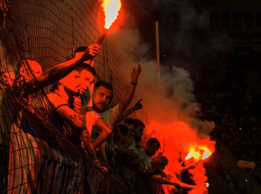 Odessa, Ukrayna -Temmuz28,2019: Fanatik taraftarlar ebedi rakipleri oyun sırasında standında. Raflarda hayranları mutlu, ateş ve bayrak sallayarak parlıyor. Stadyumda ateşli bir gösteri. Holigan ışık ateşli flaş Fan