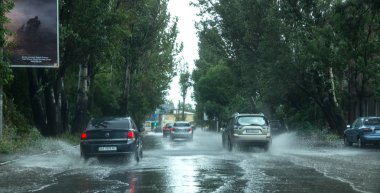 Odessa, Ukrayna -9 Ağustos 2019: sağanak yağışların neden olduğu sel felaketi sırasında su lar altında kalan yolda araba sürmek. Arabalar su üzerinde yüzüyor, sokakları su basayor. Arabaya sıçrat. Büyük bir su birikintisi ile sular altında şehir yolu