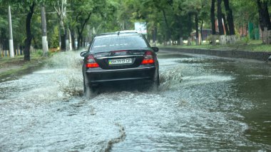 Odessa, Ukrayna -9 Ağustos 2019: sağanak yağışların neden olduğu sel felaketi sırasında su lar altında kalan yolda araba sürmek. Arabalar su üzerinde yüzüyor, sokakları su basayor. Arabaya sıçrat. Büyük bir su birikintisi ile sular altında şehir yolu